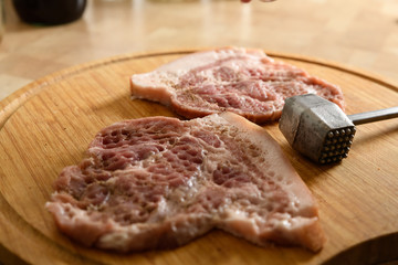 piece of pork with a meat hammer on wooden background close-up
