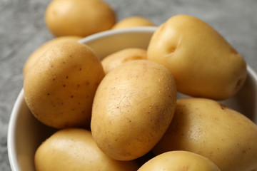Bowl with young potato on grey background, close up