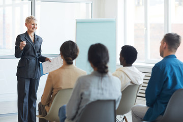 Portrait of successful mature businesswoman giving speech to audience during seminar, copy space
