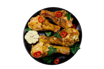 Roasted chicken drumsticks with spices in a black plate isolated on white background. Top view
