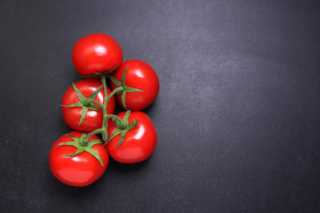Red ripe tomatoes on a branch. Vegetables on a black textured background.