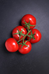 Red ripe tomatoes on a branch. Vegetables on a black textured background.