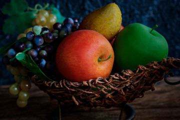 Artificial fruits lie in a wicker basket. Still life with dark lighting. Background.