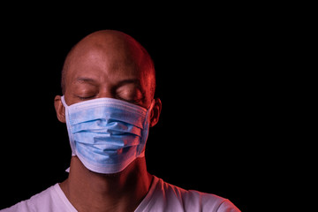 Coronavirus, portrait of a black man with protective mask and closed eyes. COVID-19 concept. Studio shot on dark background. Copy space