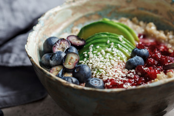 Oatmeal porridge bowl with avocado, berries and sesame. Dark background, healthy food.