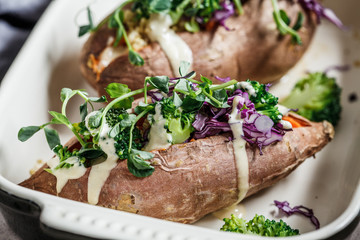 Baked sweet potatoes stuffed with quinoa, broccoli and cabbage, dark background.