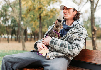 Owner holding striped cat inside his jacket, sitting on the bench in the park