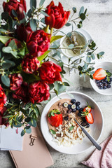 Flat lay of beautiful breakfast with granola, berries, tea and a bouquet of flowers.