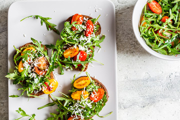 Tomatoes, arugula and cheese sandwiches on a gray plate, top view.