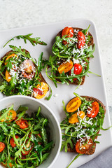 Tomatoes, arugula and cheese sandwiches on a gray plate, top view.