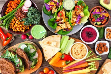 Photo sur Plexiglas Manger Healthy lunch table scene with nutritious Buddha bowl, lettuce wraps, vegetables, sandwiches and salad. Above view over a wood background.