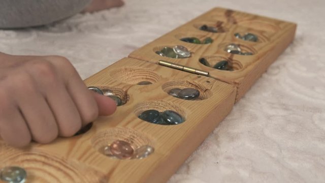 old intelligence games, wooden mancala game, a person playing mancala,