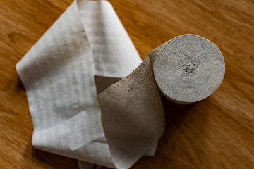 A roll of clean, plain toilet paper, cheap quality, dirty color, lies on a brown wooden table,...