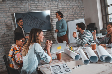 Group of modern business people in casual wear discussing architectural designs while sitting in the creative office.