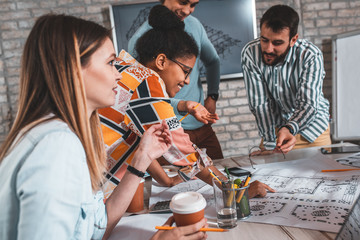 Group of modern business people in casual wear discussing architectural designs while sitting in the creative office.