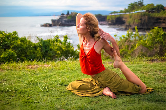 Outdoor yoga practice. Young woman practicing Eka Pada Rajakapotasana, One Legged King Pigeon Pose. hest opener improving breathing. Tanah Lot temple, Bali, Indonesia