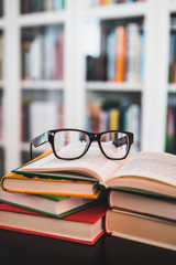 Glasses on stack of books. Library in the background. Books and glasses.