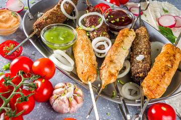 Summer bbq party. Shish kebab on a stick, from ground beef and chicken meat. Lula kebab, traditional Caucasian asian dish. With various sauces, spices and tomatoes, grey stone background, copy space a
