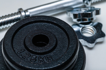 Obraz na płótnie Canvas Close-up of four black weight training weights in focus stacked upon each other with handle and locks out of focus on a white background. Concept of training, fittness and excercise for healthy living