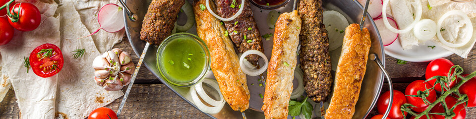 Summer bbq party. Shish kebab on a stick, from ground beef and chicken meat. Lula kebab, traditional Caucasian asian dish. With various sauces, spices and tomatoes, grey stone background