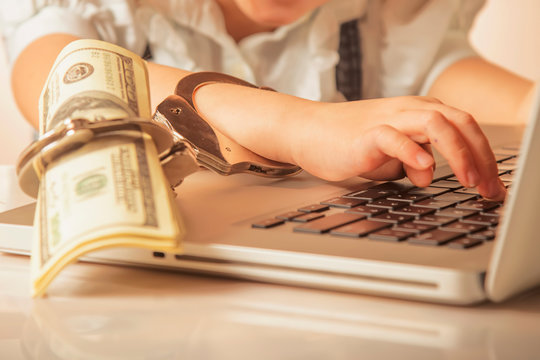 Slave of work, success and money concept. Close up handcuffed persons hand on laptop with US Dollar. Selective focus hends and finger.