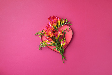 Spring freesia flowers over red heart on pink background. Top view. Flat lay. Summer and spring...