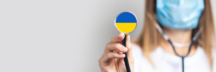 female doctor in a medical mask holds a stethoscope on a light background. Added flag of Ukraine....