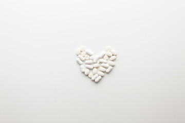 White background with scattered tablets in the shape of a heart. Medical background. Minimal composition. Copy space