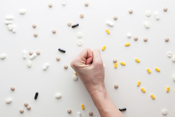 White background with scattered tablets. A clenched female hand. Medical background. Fighting the epidemic.