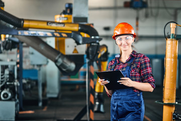 Pretty female student with Hard Hats and protective glasses doing practical work at industrial factory and smile