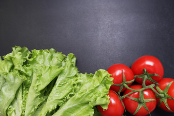 Green lettuce leaves red ripe tomatoes on a branch. Vegetables on a black textured background.