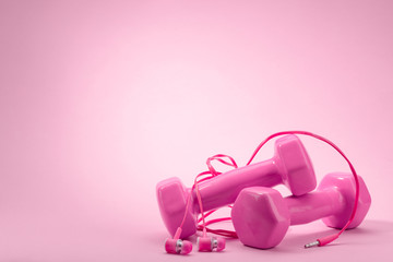 Dumbbells and in-ear headphones on pink background
