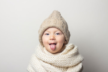 beautiful little baby in a hat shows tongue on a light background. Concept of children's emotions, winter, shopping