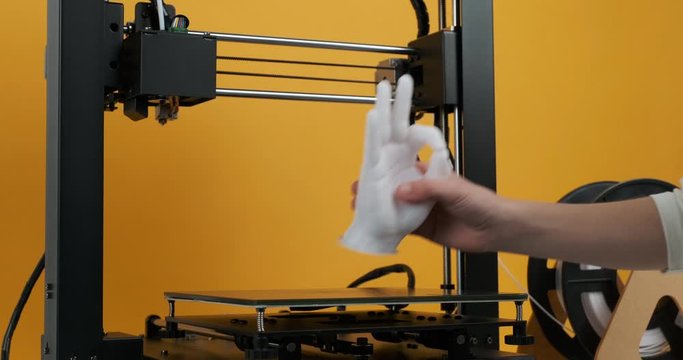 Close-up 3D printer printed model hands fingers ok sign made white plastic yellow background. Boy looks at model hands and picks up from printer platform. Potential of modern 3D printing technology
