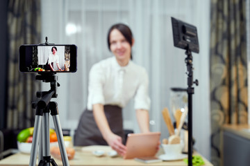 Vlogger freelance job, food concept. Young caucasian woman cooking and recording live video for vlog and social media with phone camera in their kitchen