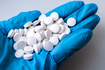 рука доктора в синей медицинской перчатке держит горсть таблеток