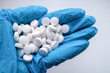 рука доктора в синей медицинской перчатке держит горсть таблеток