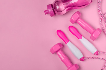 Jump rope, bottle of water and dumbbells on pink background