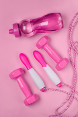 Jump rope, bottle of water and dumbbells on pink background
