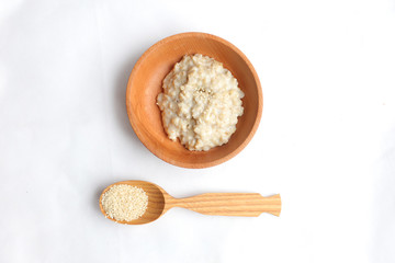 Oatmeal in a wooden bowl and dry berries in a bag. near a wooden spoon with sesame seeds on a white background. breakfast