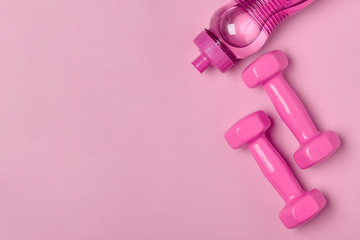 Bottle of water and dumbbells on pink background