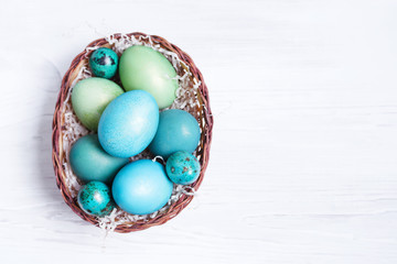Bright Easter eggs in a basket on a white wooden surface, top view. Easter background.	