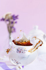 Flying black tea and levitating white cup on the purple background