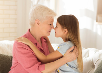 Lovely little girl and her grandma touching noses and embracing at home