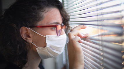 Corona Virus Quarantine Isolation. Sick woman of corona virus looking through the window and wearing mask protection and recovery from the illness in hom