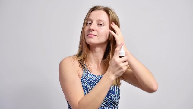 Blond woman with wet hair is spritzing liquid from spray bottle