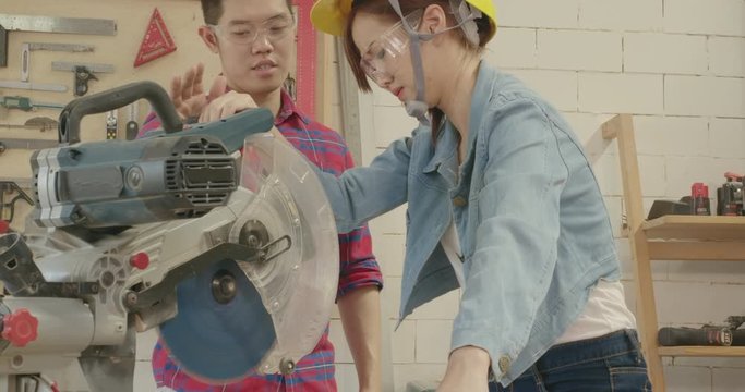 Training woodworker coaching carpentry trainee using cutting machine wood in a industry workshop office, Male carpenter supervise woman apprentice learning for safety  between working concept.