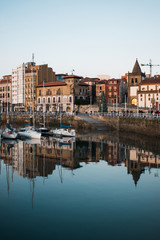 Fototapeta na wymiar Barrio de Cimadevilla y barcos de vela reflejados en las aguas del puerto en una tarde tranquila