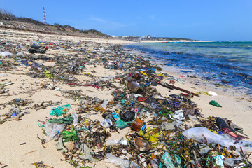 A view along a sandy beach full of plastic garbage.