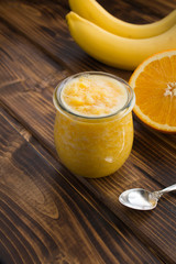Smoothies or puree  with orange and banana in the small glass jar on the brown wooden  background.  Location vertical.